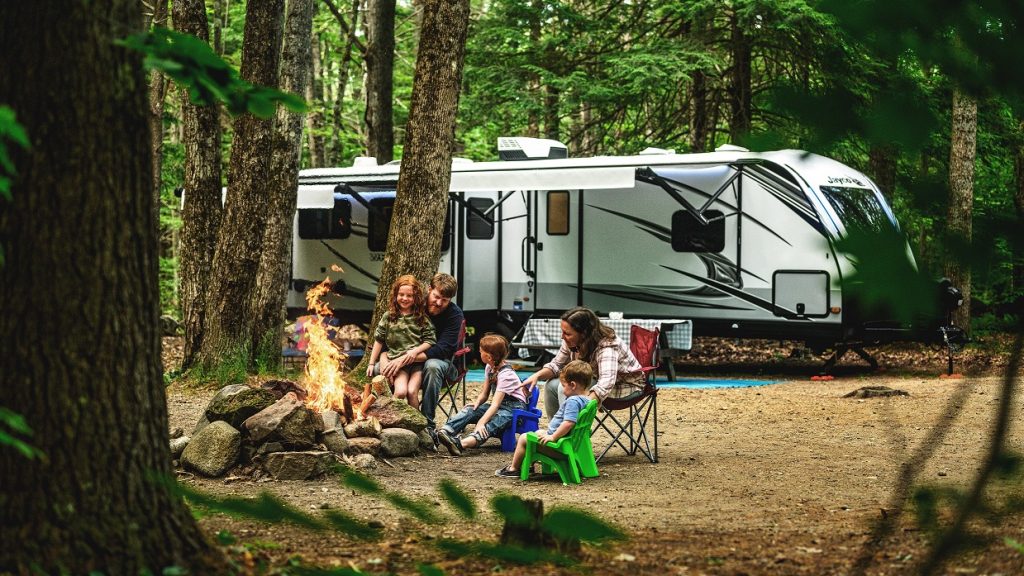 Family sitting by a campfire with a camper in the background