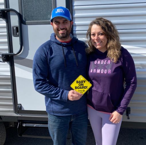 Man with arm around wife with Baby on Board sign