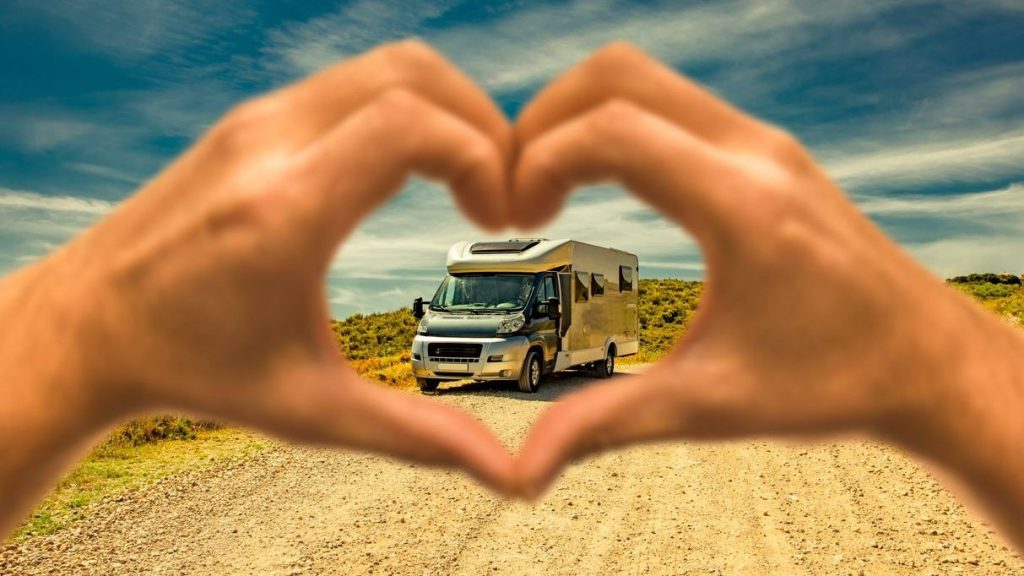 Hands making a heart with a class c rv in the background