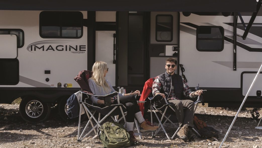 couple sitting outside a grand design imagine rv