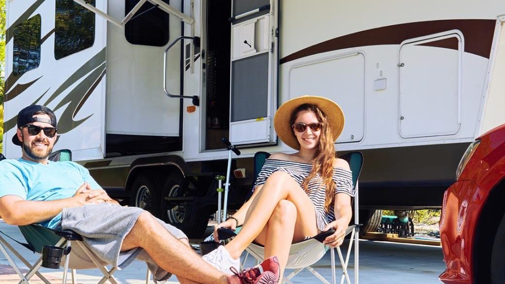 young couple outside camper sitting in camp chairs