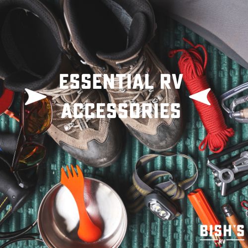 Overhead view of essential RV accessories including hiking boots, rope, utensils, and tools. Text overlay reads 'ESSENTIAL RV ACCESSORIES' with Bish's logo.