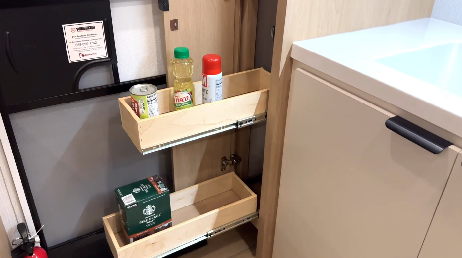 RV kitchen pull-out pantry cabinet with two wooden shelves holding canned goods, cooking oil, and Starbucks coffee pods.









