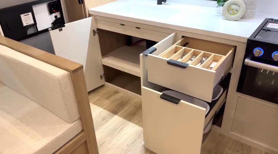 RV kitchen pull-out pantry cabinet with two wooden shelves holding canned goods, cooking oil, and Starbucks coffee pods.









