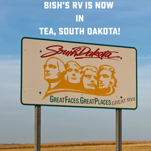 A road sign welcoming travelers to South Dakota, featuring an illustration of Mount Rushmore with the state slogan “Great Faces. Great Places.” The design has been humorously edited to add “GREAT RVs” in small text. Above the sign, bold white text reads: “BISH’S RV IS NOW IN TEA, SOUTH DAKOTA!” against a partly cloudy blue sky backdrop.