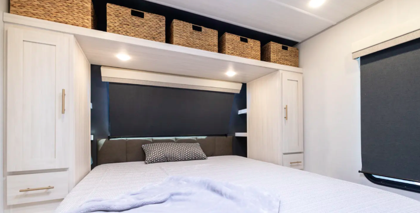 R-Pod Unmapped travel trailer bedroom with Olympic queen bed, overhead storage baskets, built-in wardrobes, and side windows with blackout shades.
