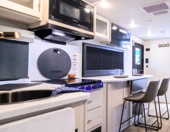Modern R-Pod Unmapped travel trailer kitchen with microwave, stove, extended counter bar seating, and large window for natural light.