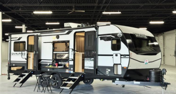 Forest River R-Pod Unmapped travel trailer displayed indoors with slide-outs extended and exterior kitchen open, featuring a modern white and black design.