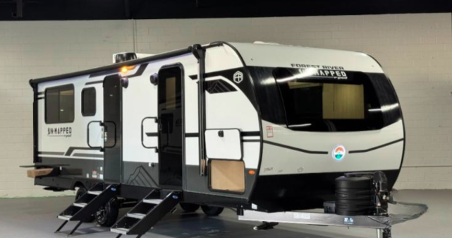 A Forest River R-Pod Unmapped travel trailer with a modern white and black exterior, extended entry steps, large front window, and dual axles, displayed indoors under bright lighting.