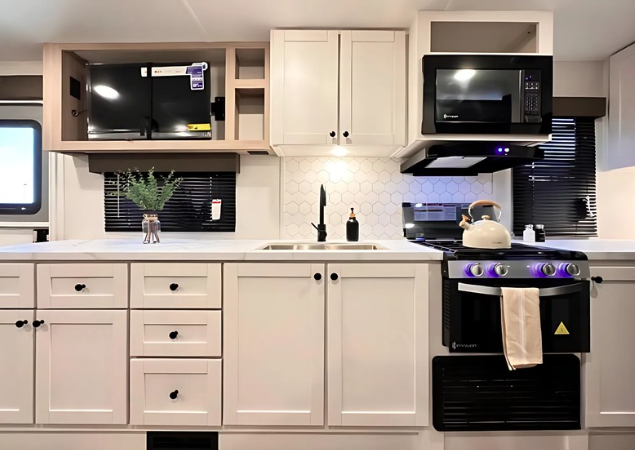 White Wayfinder Go Explore Limited travel trailer with sleek black accents and large panoramic front window, parked on pavement with green trees in the background.
