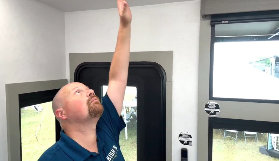 Josh the RV Nerd inside the Axiom Imperium 12900 RV demonstrating the exceptionally tall ceiling height by reaching upward near the entryway and panoramic windows.