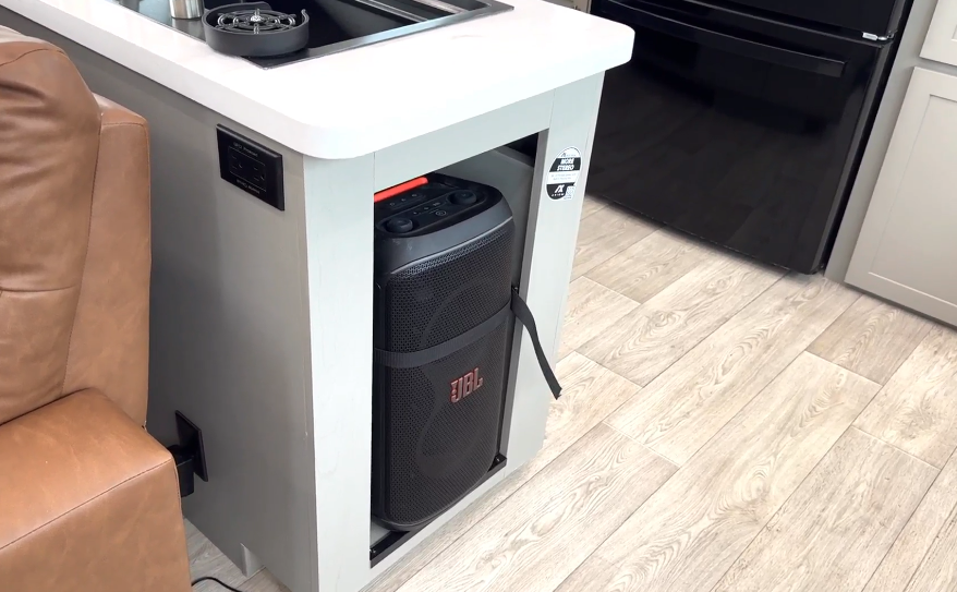 Axiom Imperium 12900 fifth wheel RV kitchen with built-in JBL Bluetooth speaker storage, solid surface countertop, and modern cabinetry.