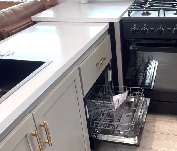 Axiom Imperium 12900 RV kitchen with built-in dishwasher, gas oven, solid surface countertops, and modern cabinetry with gold hardware.
