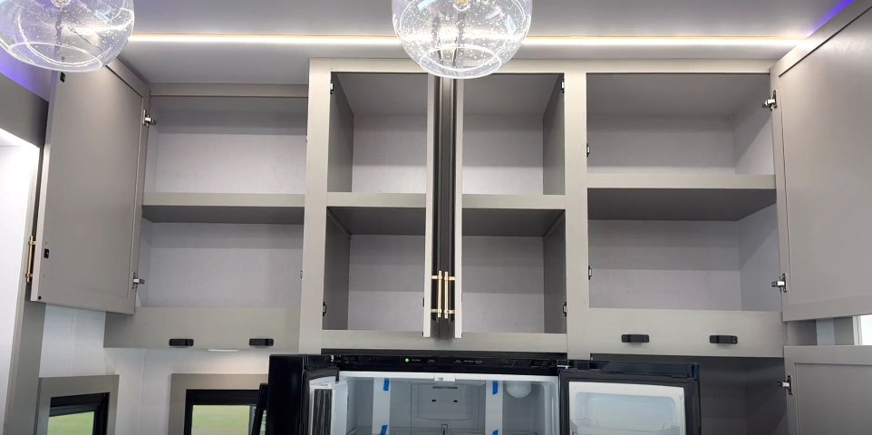 "Spacious overhead kitchen cabinets with modern brushed gold handles inside the Axiom Imperium 12900 fifth wheel RV, offering abundant storage above the residential refrigerator.