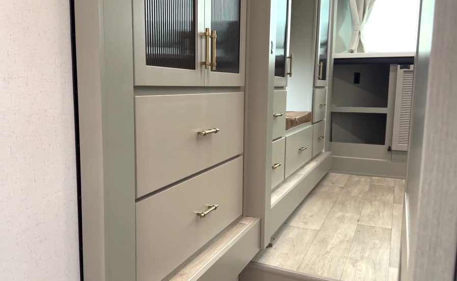 Hallway storage cabinets and wardrobe with modern gold hardware inside the Axiom Imperium 12900 RV, offering built-in drawers, closet space, and a seating bench.