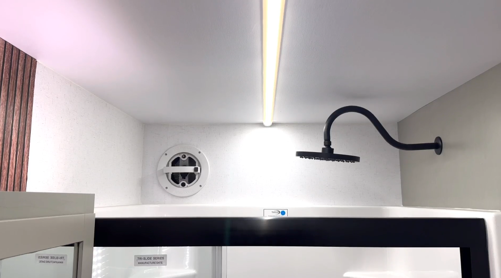 Modern RV bathroom shower in the Axiom Imperium 12900 featuring a black rainfall showerhead, LED ceiling lighting, and contemporary wall finishes.