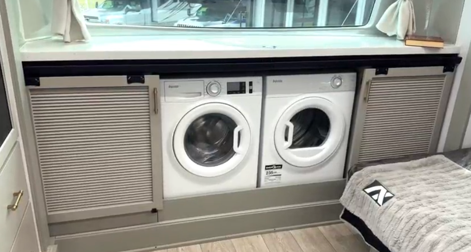 Luxury RV bedroom in the Axiom Imperium 12900 featuring built-in washer and dryer units with sliding cabinet doors beneath a large window