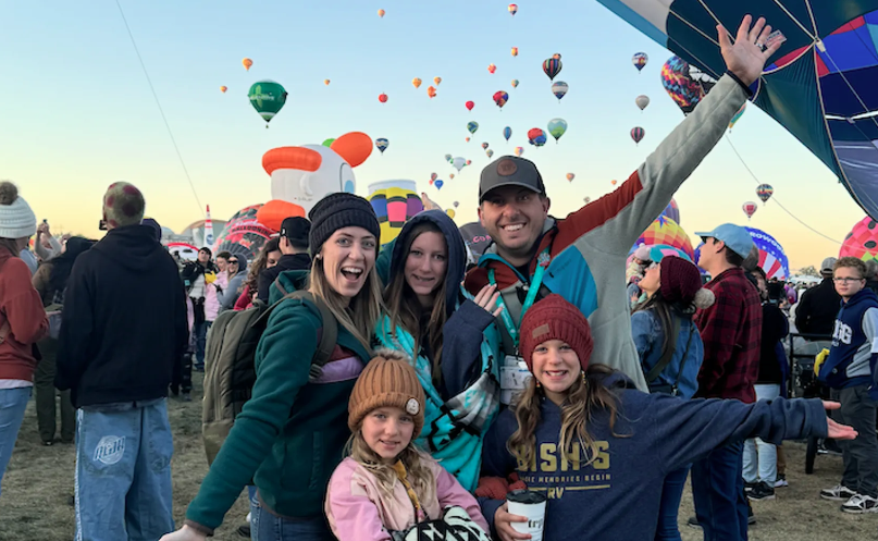 Family enjoying the Albuquerque International Balloon Fiesta, smiling in front of colorful hot air balloons filling the sky
