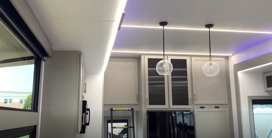 Luxury RV kitchen in the Axiom Imperium 12900 featuring modern pendant lighting, overhead cabinets, full-size refrigerator, and sleek contemporary design.