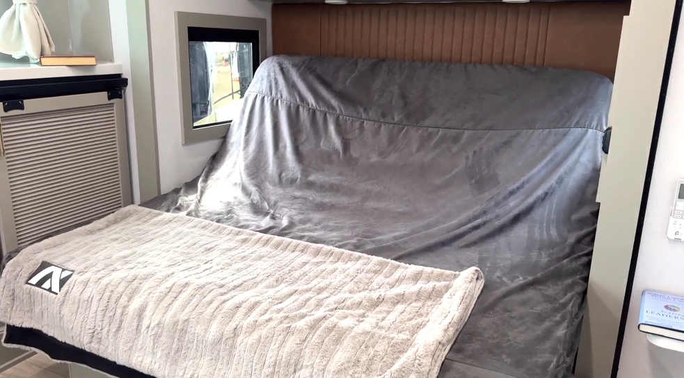 Bedroom in the Axiom Imperium 12900 fifth wheel RV featuring a large bed with plush gray bedding, side windows for natural light, and built-in cabinetry.