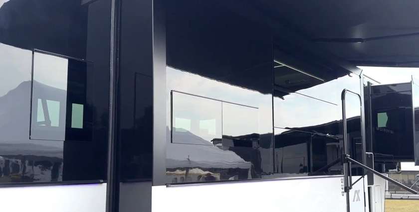 Close-up of the sleek black fiberglass sidewall and tinted windows on the Axiom Imperium 12900 fifth wheel RV, highlighting its modern luxury exterior design.