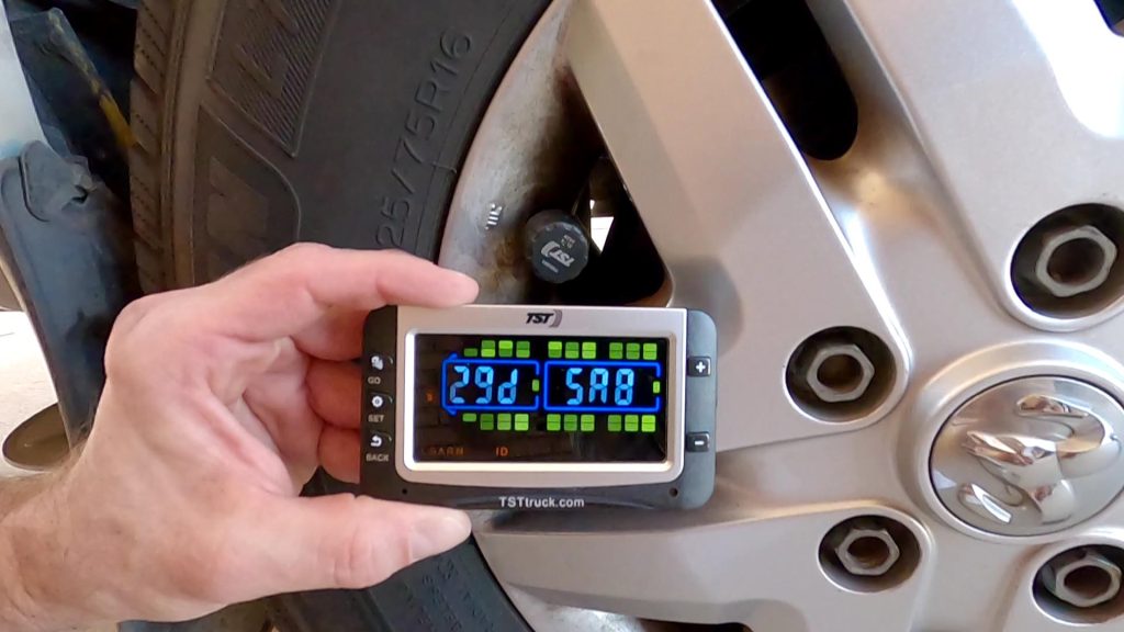 Close-up of a tire pressure monitoring system (TPMS) gauge showing 29 PSI and 58 degrees Fahrenheit while connected to a vehicle tire valve stem, ensuring safe RV and trailer travel