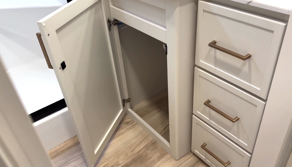 Open vanity storage in the Brinkley Model I 280 bathroom showcasing a deep lower cabinet and three soft-close drawers with brushed gold handles. The design offers ample space for toiletries and towels while maintaining the RV’s clean, residential aesthetic.