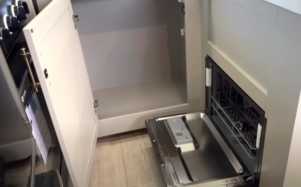 Open cabinet and built-in dishwasher inside the 2026 Axiom Imperium I3800 kitchen, highlighting premium GE appliances, ample lower storage, and modern RV interior finishes.