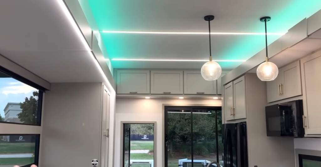 Ceiling view of the 2026 Axiom Imperium I3800 kitchen showcasing LED accent lighting, modern pendant fixtures, overhead cabinets, and sliding glass doors for a bright, contemporary RV interior design.