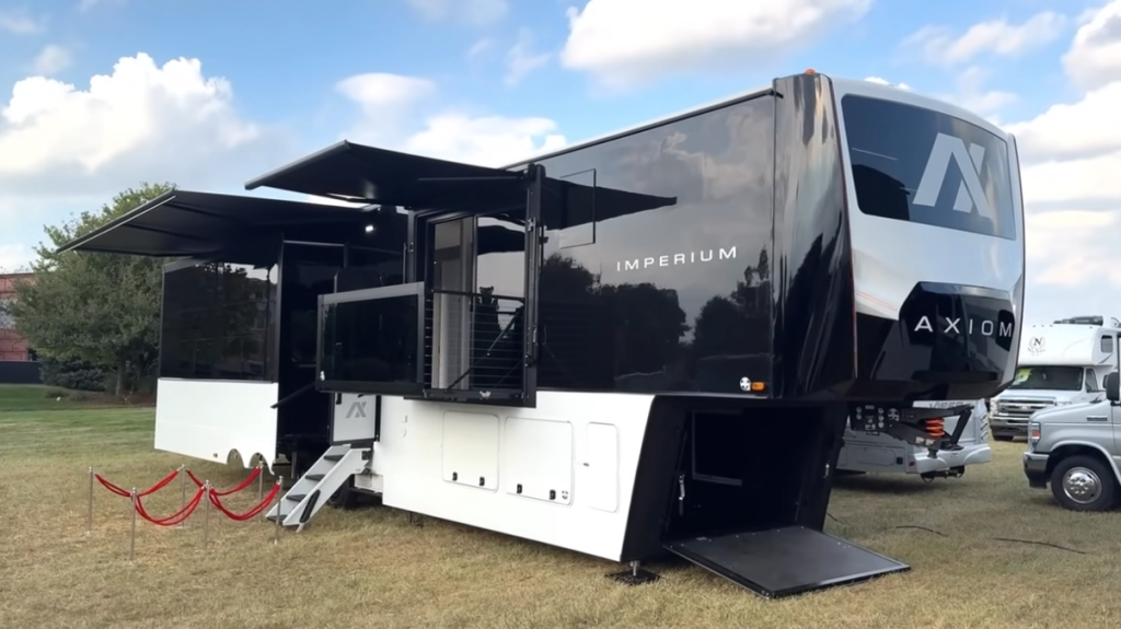 2026 Axiom Imperium I3800 fifth wheel RV on display with extended slides, rear patio deck, and black-and-white exterior design under a partly cloudy sky, showcasing luxury construction and modern steel-framed architecture.