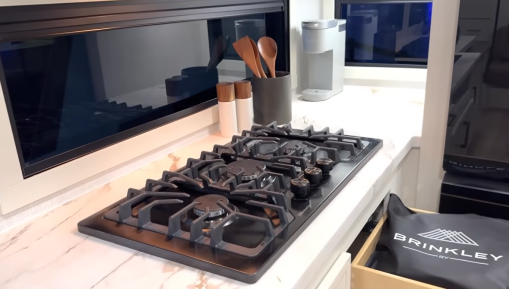 Brinkley Model Ix 20X kitchen cooktop with three-burner sealed stove, marble-look countertop, panoramic window, and modern utensil holder for a sleek residential RV design.