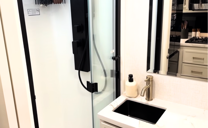 Brinkley Model Ix 20X bathroom with luxury fiberglass shower, black matte fixtures, marble-look vanity, and gold faucet for a modern residential RV design.