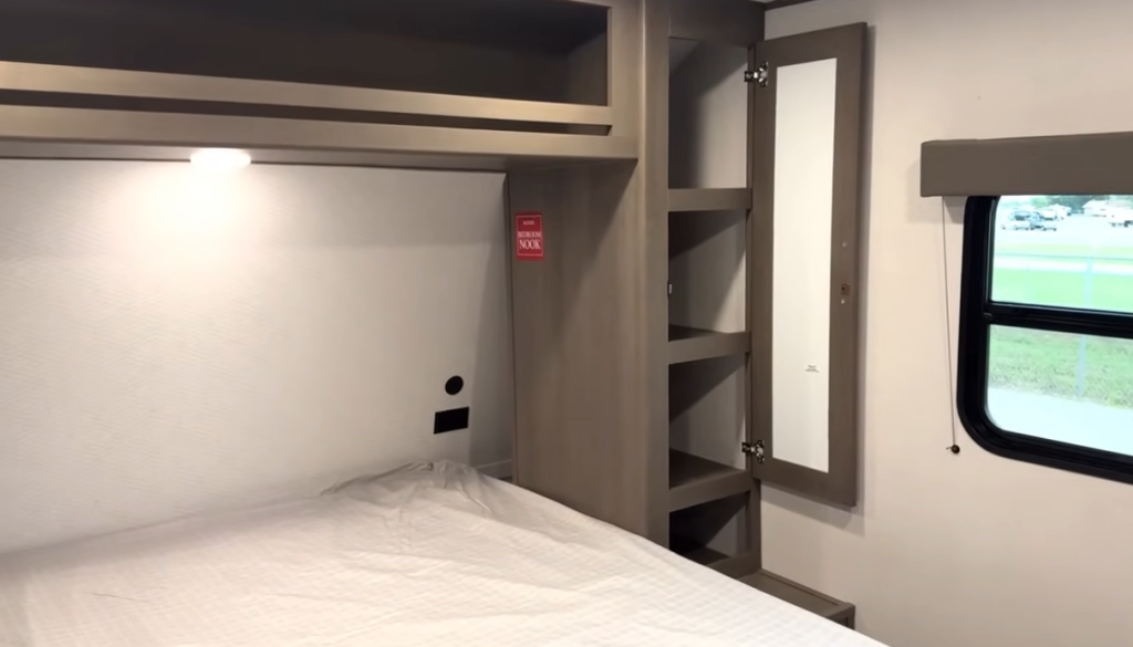 Grand Design Transcend Xplor 22RBX bedroom with overhead storage, side shelving, mirrored wardrobe, and window for natural light.