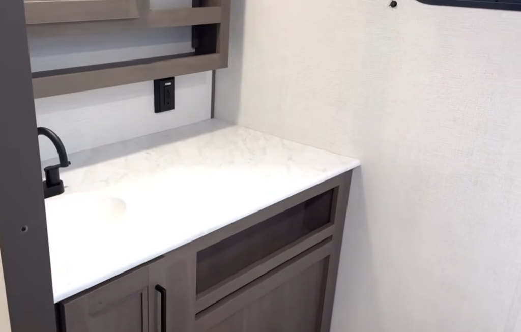 Grand Design Transcend Xplor 22RBX bathroom vanity with marble-look countertop, black faucet, storage cabinets, and wall outlet.