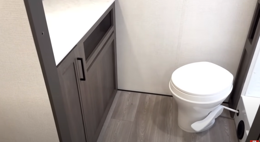 Grand Design Transcend Xplor 22RBX bathroom with modern vanity, white foot-flush toilet, and wood-look vinyl flooring.