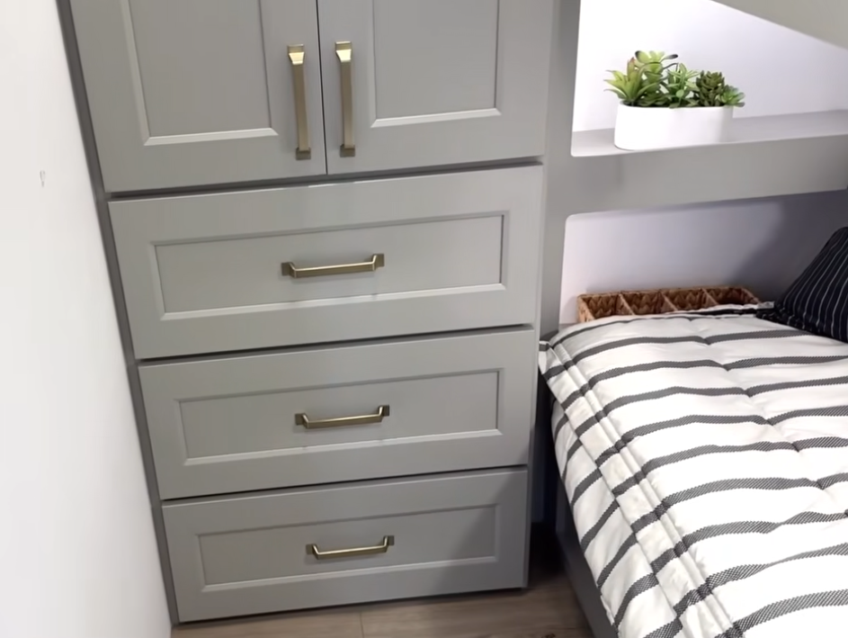Brinkley Model G Series RV bunkroom featuring built-in dresser storage with gold hardware beside a cozy striped bedding setup and decorative shelving, showcasing smart space utilization and modern design.