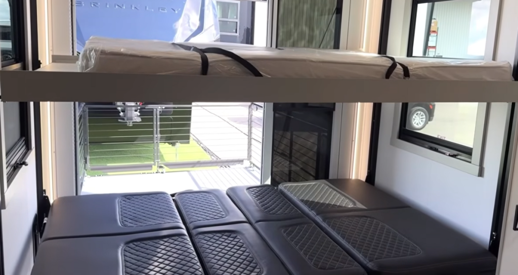 Brinkley Model G Series RV garage with Happy-Jack lift system, featuring fold-down bench seating that converts to a bed and an overhead bunk, offering flexible sleeping and lounge options for guests or gear.