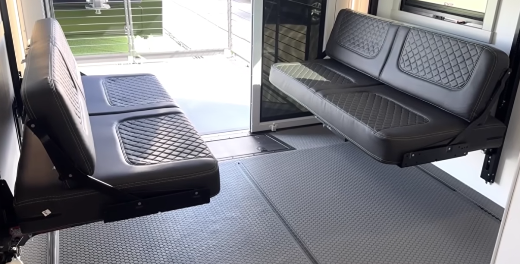 Brinkley Model G Series RV garage showing fold-down HappiJac benches with diamond-stitched upholstery, offering convertible seating or sleeping space and easy access to the rear patio ramp.
