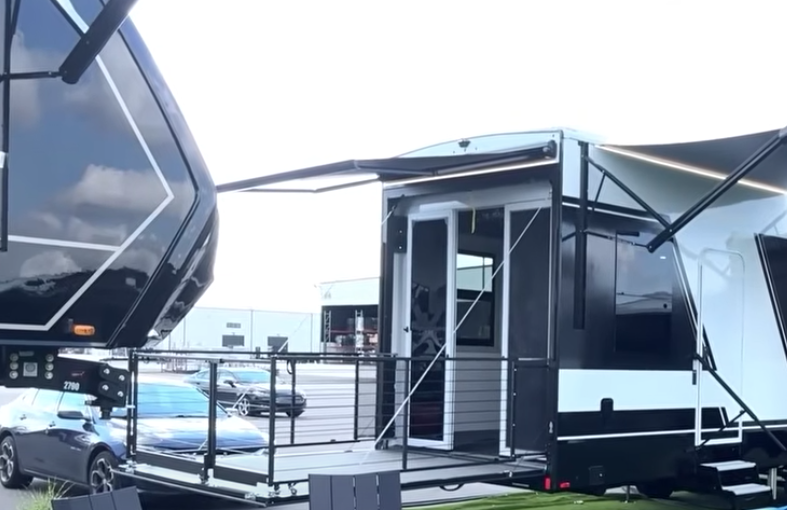 Brinkley Model G Series luxury toy hauler exterior showcasing rear patio deck with railing system, dual awnings, and modern black-and-white body design for outdoor lounging and entertainment.