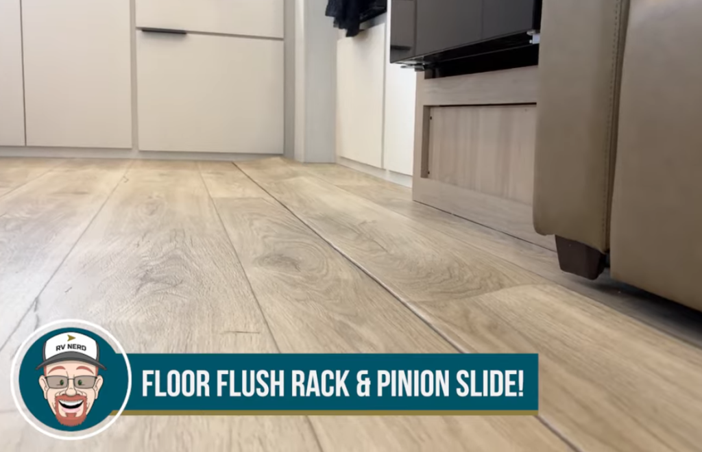 Close-up of the 2026 Winnebago Thrive 22MLS floor flush rack and pinion slide system showing seamless wood-look flooring and smooth transition between living areas.