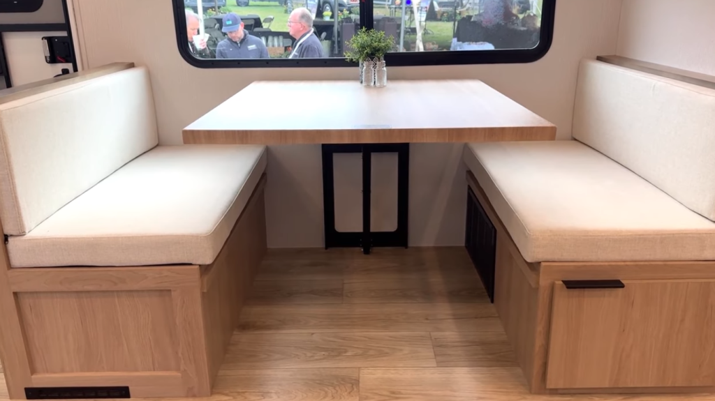 2026 Winnebago Thrive 22MLS dinette with light wood table, dual cushioned bench seating, under-seat storage, and large window for natural light and campground views.
