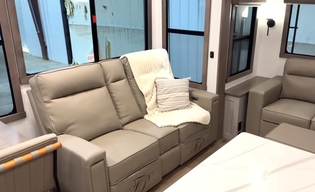 Alliance Paradigm RV living area with dual power recliners, tan leather seating, throw blanket, and striped accent pillow, showcasing a cozy and modern residential lounge design