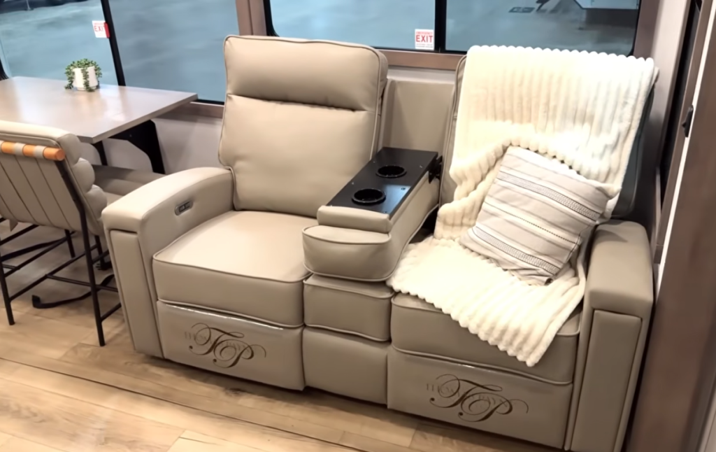 Alliance Paradigm RV living area with dual reclining theater seats, center console with cupholders, cream throw blanket, and striped accent pillow beside the freestanding dinette.