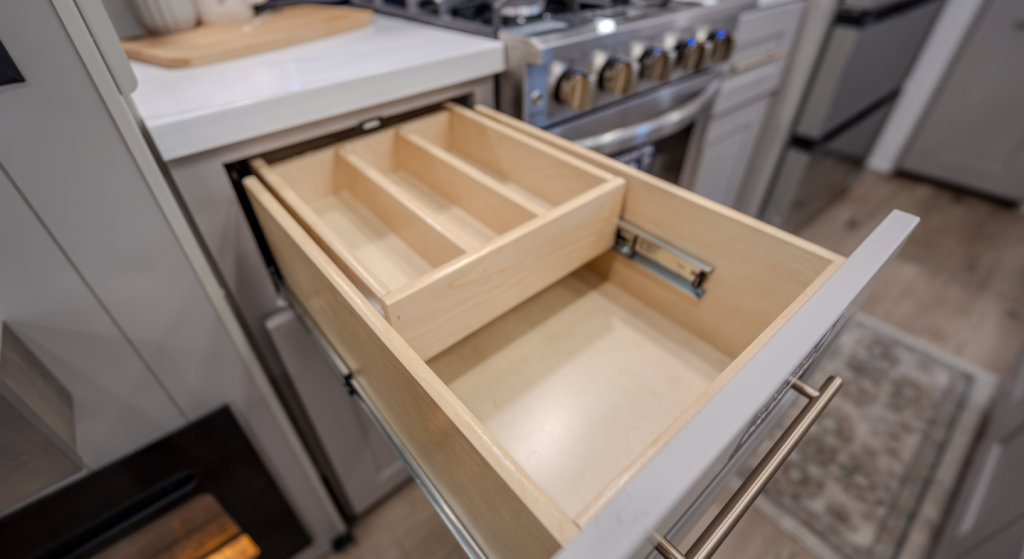 Alliance Paradigm fifth wheel kitchen drawer with built-in utensil organizer and soft-close slides, positioned beside the residential gas range and solid-surface countertops.