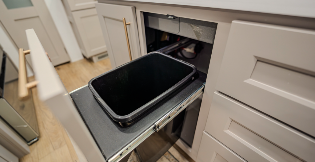 Alliance Paradigm fifth wheel kitchen featuring a pull-out trash can drawer with modern cabinetry and gold hardware for easy waste storage and a clean, organized look.