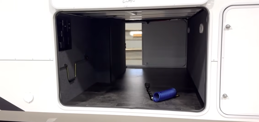 Alliance Paradigm fifth wheel pass-through storage compartment with clean finished walls, tie-down hooks, and included hose and accessories for RV setup.