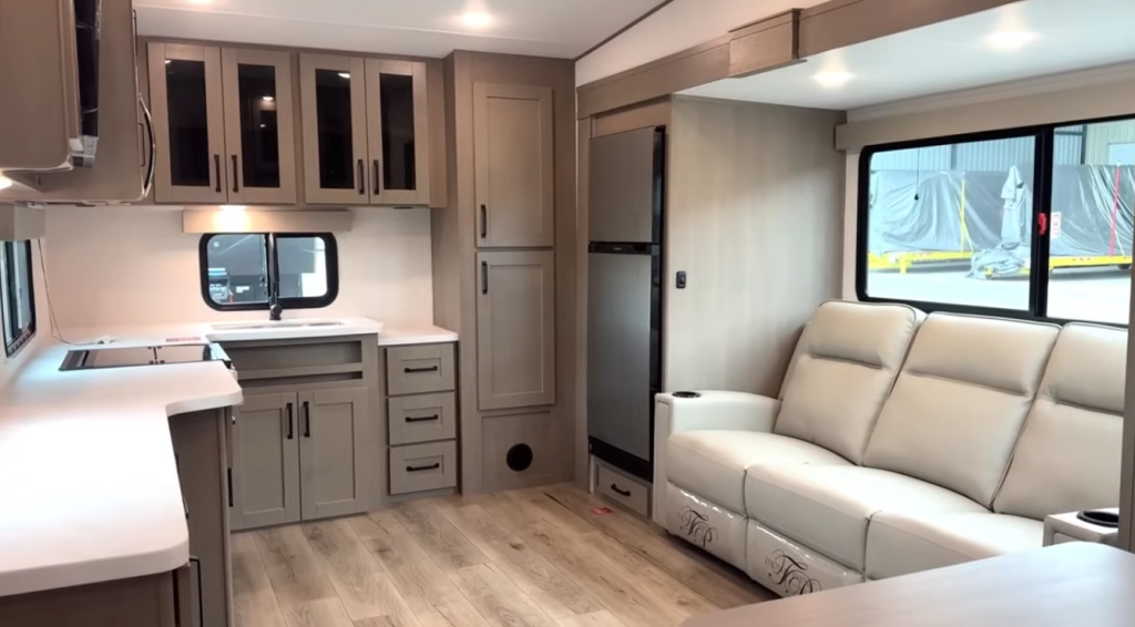 2026 Grand Design Reflection 150 270BN interior featuring a rear kitchen layout with ample cabinetry, stainless steel refrigerator, and light leather theater seating in a modern open-concept design.