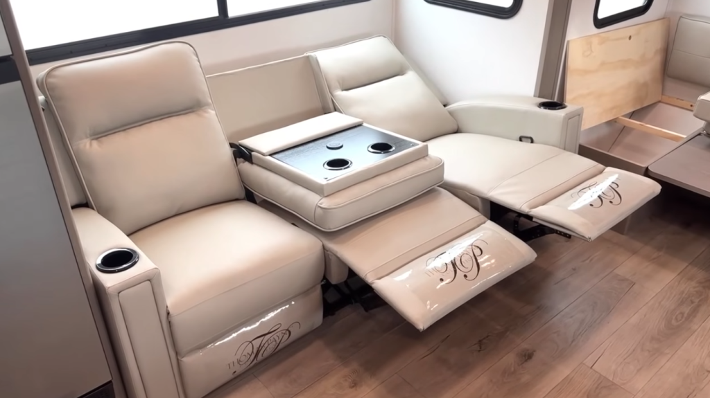 2026 Grand Design Reflection 150 270BN living area with dual reclining theater seats, center console with cup holders, and modern wood-look flooring for a cozy entertainment space.