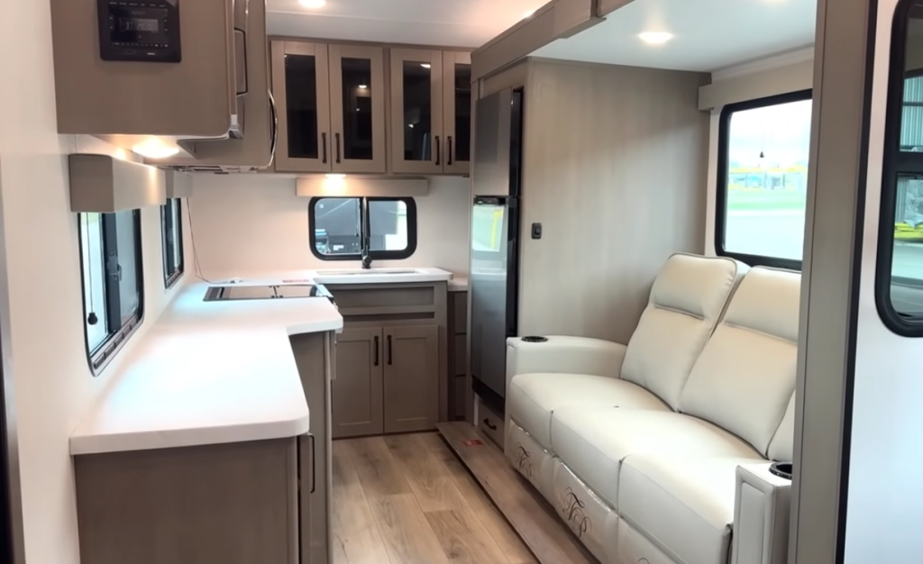2026 Grand Design Reflection 150 270BN interior showcasing spacious rear kitchen layout, solid-surface countertops, large windows, and dual recliners in a bright modern living space.