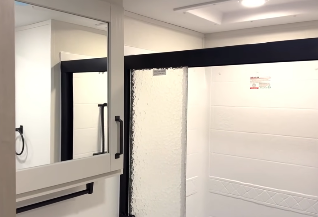 2026 Grand Design Reflection 150 270BN bathroom with glass shower enclosure, skylight for added headroom, and mirrored medicine cabinet in a bright, modern layout.